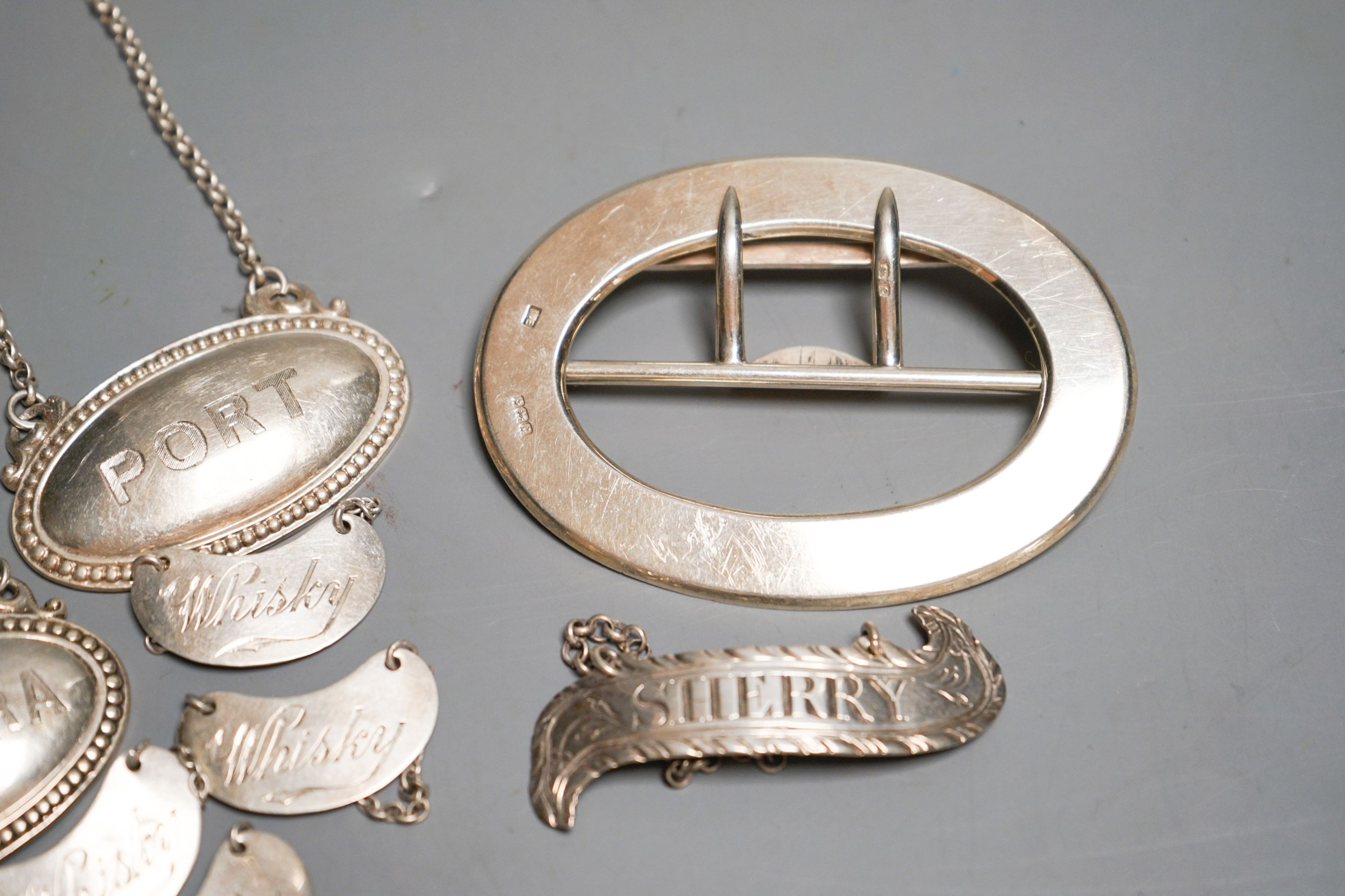 Eight assorted mainly 20th century silver wine labels and a n Edwardian silver belt buckle, 98 grams.